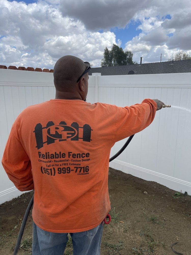 Worker in orange shirt pointing at a white fence in a yard under cloudy sky