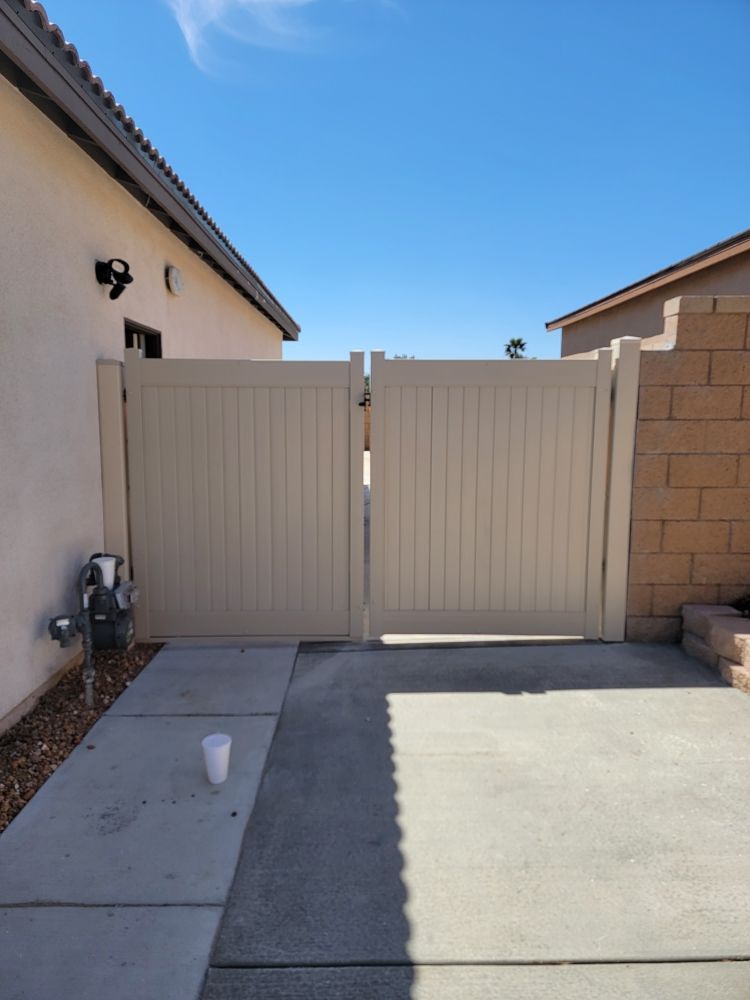 Beige double gate between two houses beside a concrete driveway under a clear blue sky