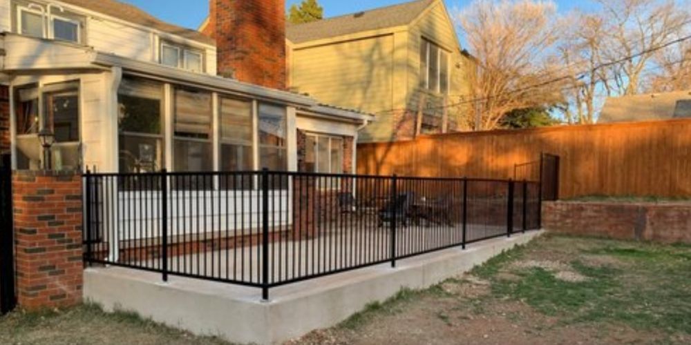 Back patio with black metal railing, brick house exterior, and lawn in warm sunlight