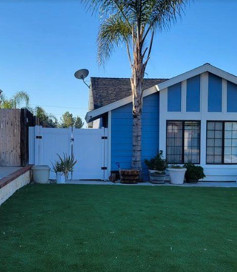 Blue house with white trim, palm tree, and green lawn under a clear sky