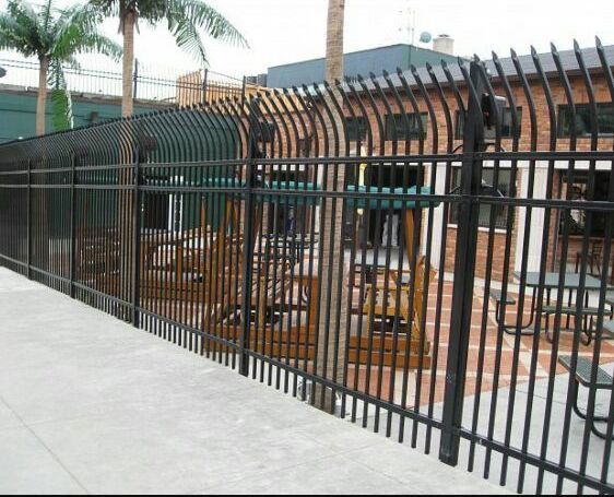Black metal fence around an outdoor patio with tables and chairs beside a building