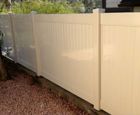 Beige vinyl privacy fence along a gravel yard with trees in the background