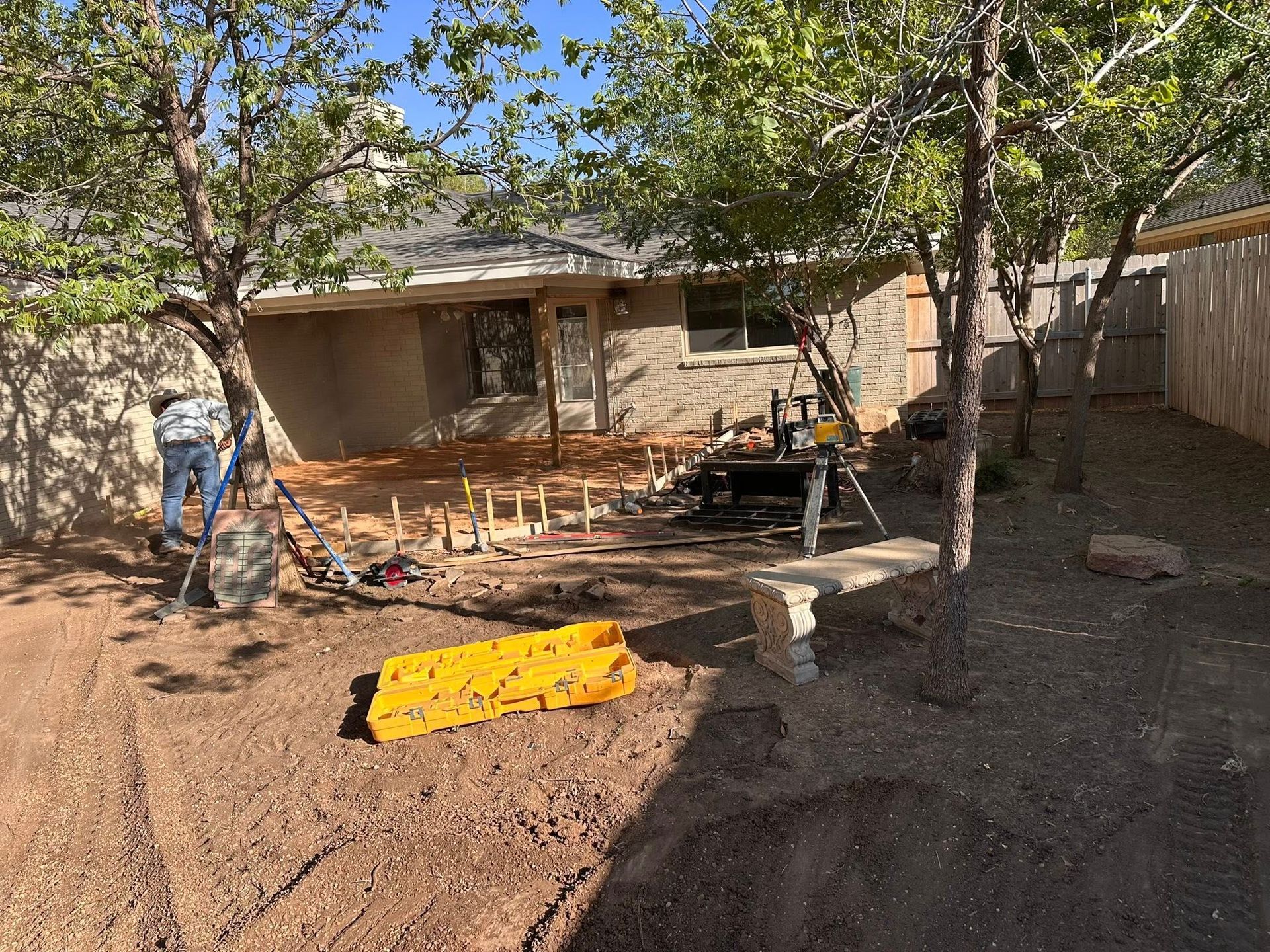 Dusty backyard with trees, a house, chairs, and a yellow tarp on the ground.