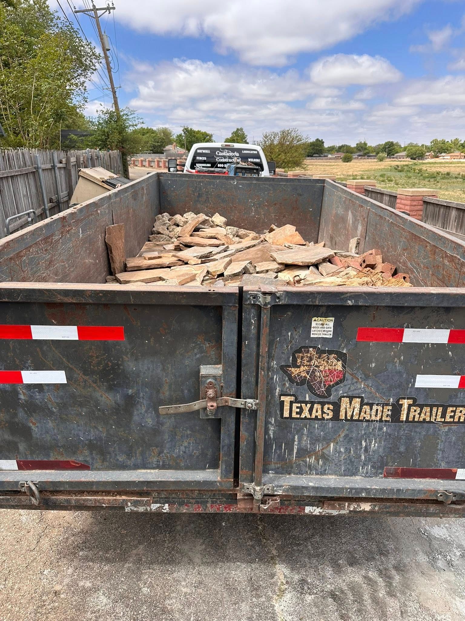 Black Texas dump trailer filled with broken bricks and debris on a roadside