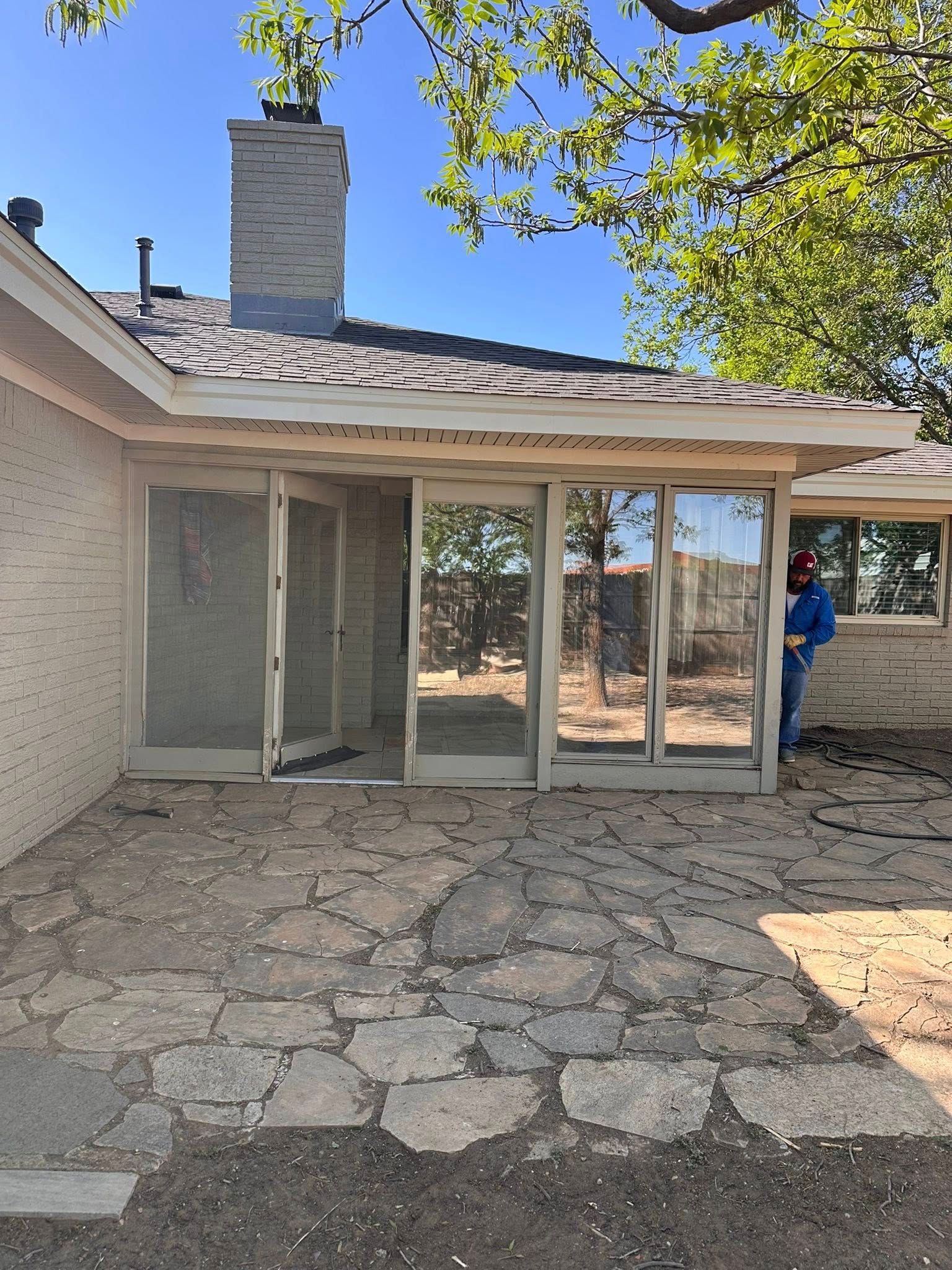 Stone patio outside a beige house with sliding glass doors and a fireplace chimney