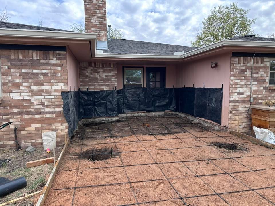 Patio under construction with rebar grid and black plastic against a brick house entrance