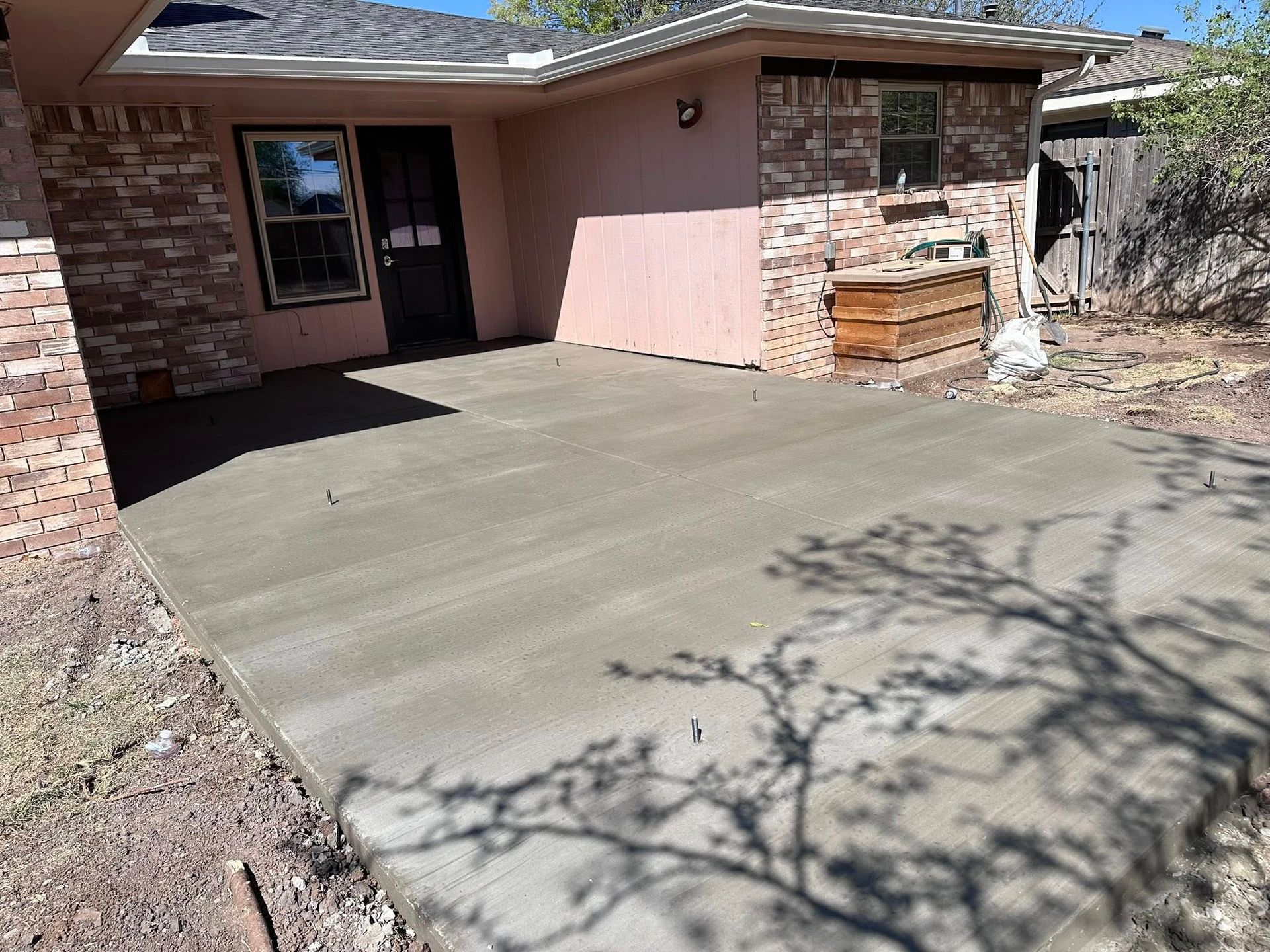 Fresh concrete patio beside a brick house with a shaded doorway and pink paneling