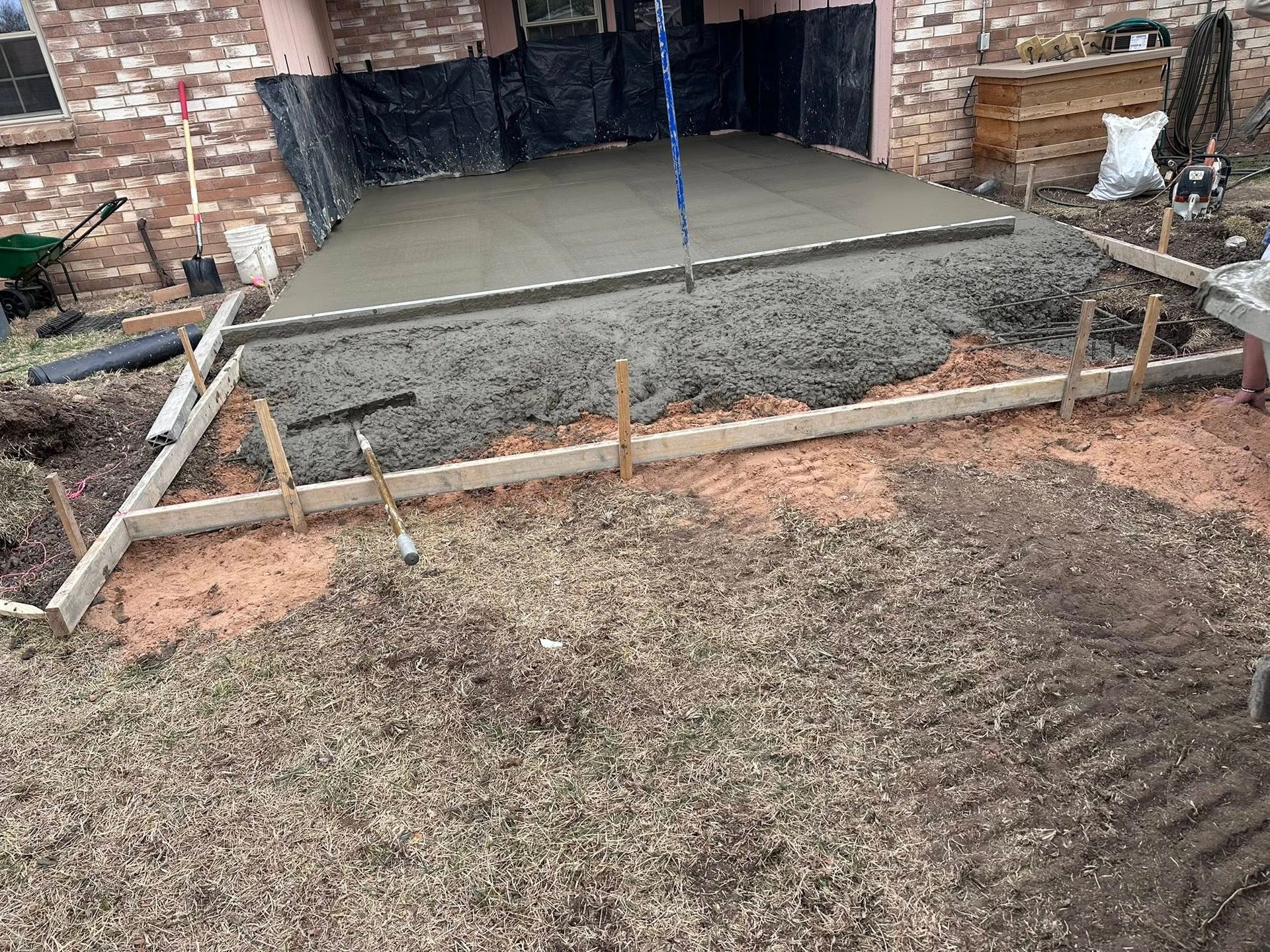 Fresh concrete slab being poured in a backyard beside a brick house