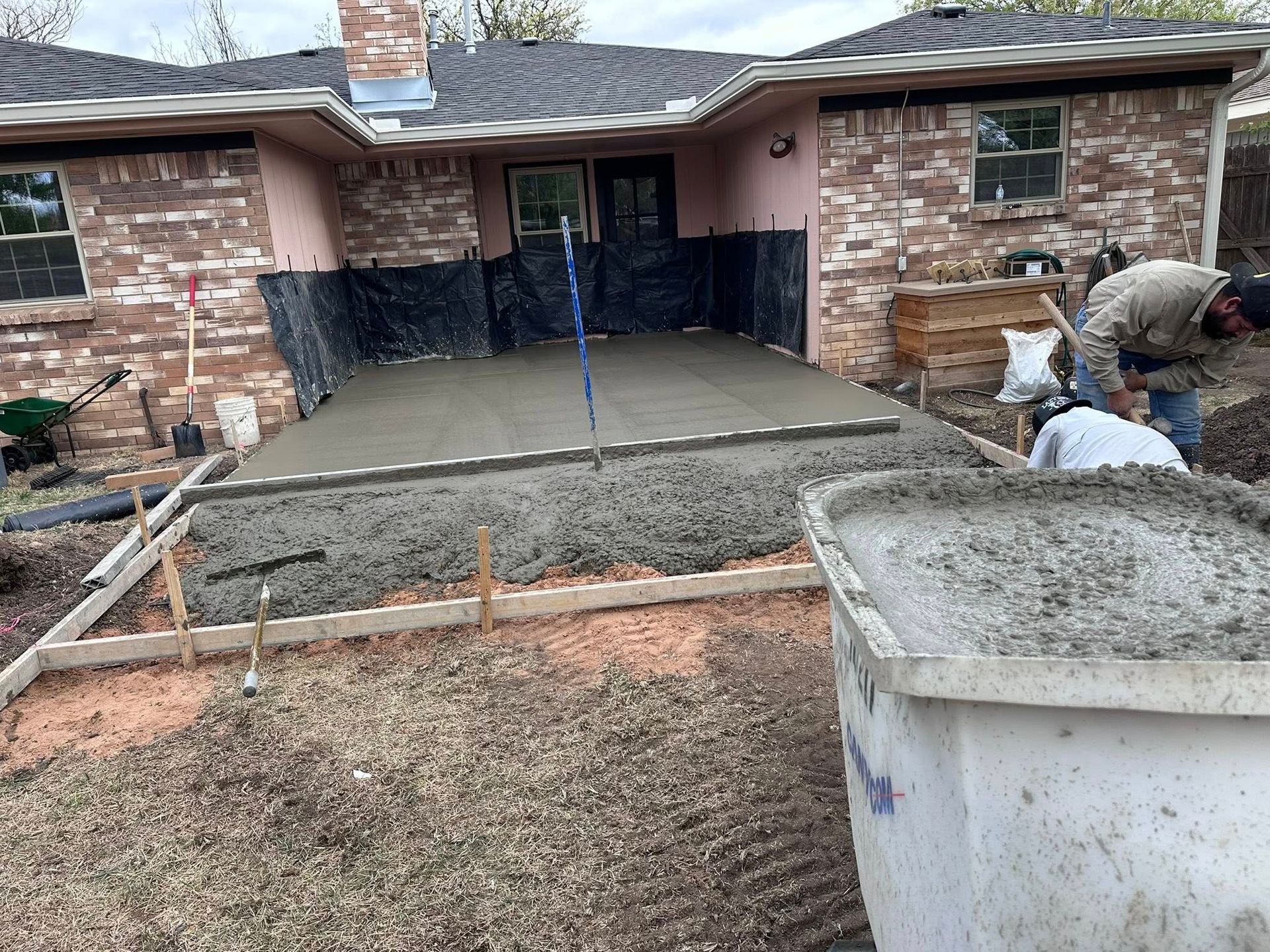Fresh concrete driveway slab being poured in front of a brick house, with workers smoothing it.
