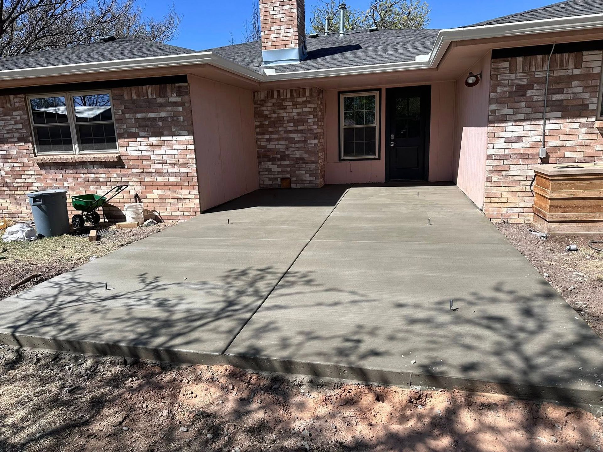 Front entrance of a brick house with a concrete driveway and covered porch, in bright sunlight.