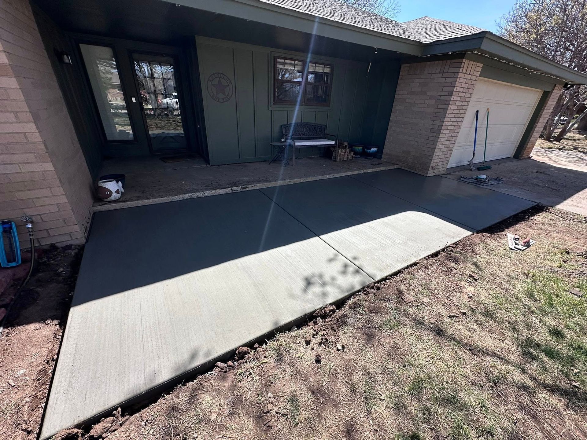 Front porch with new concrete ramp leading to a house entrance, partly shaded by the roof.