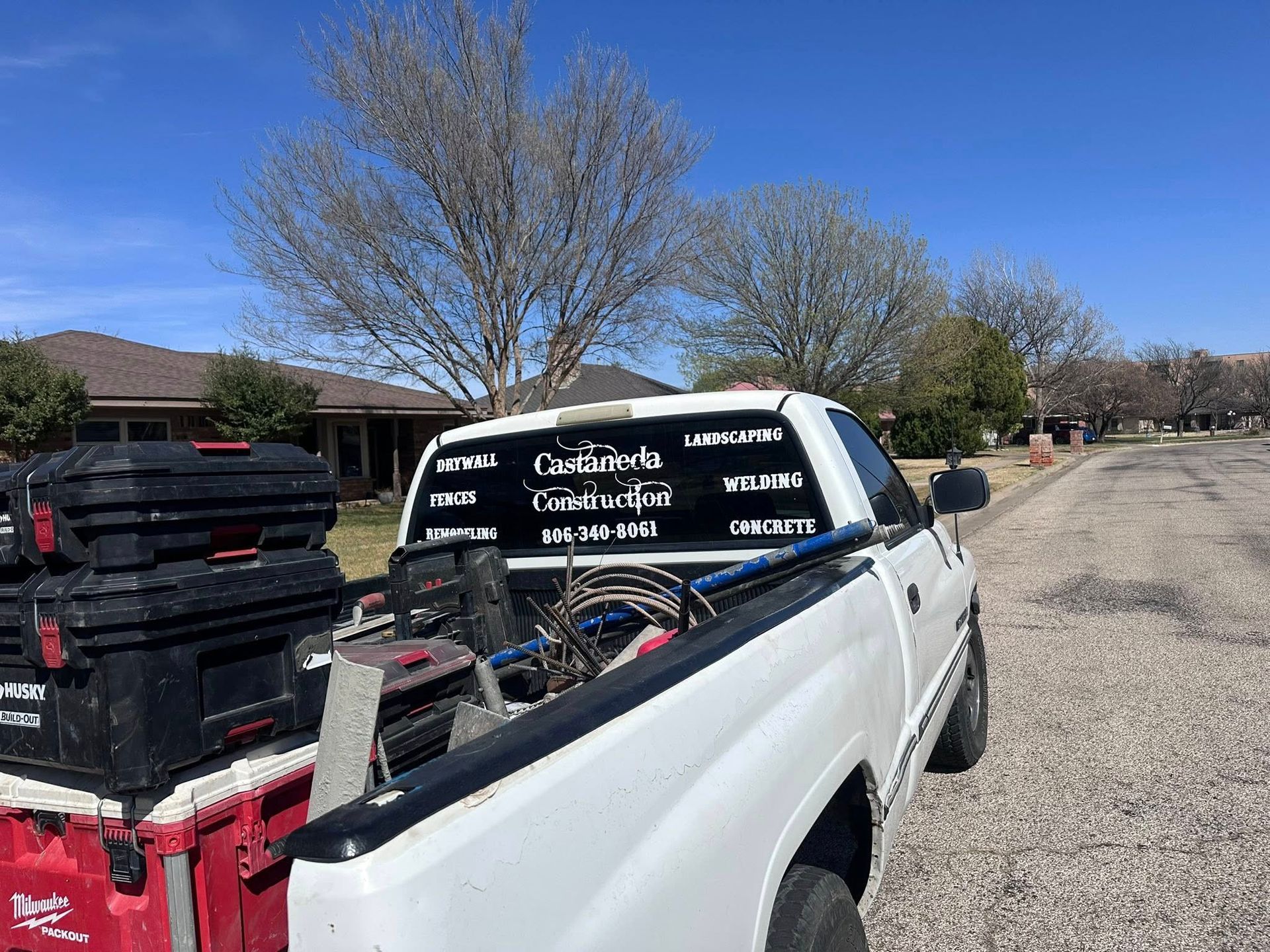 White pickup truck loaded with tools and stacked bins parked on a gravel street in a sunny neighborhood