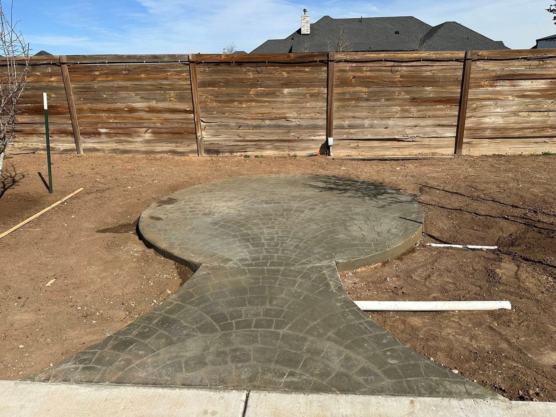 Backyard with a circular concrete patio and narrow path leading to a wooden fence.