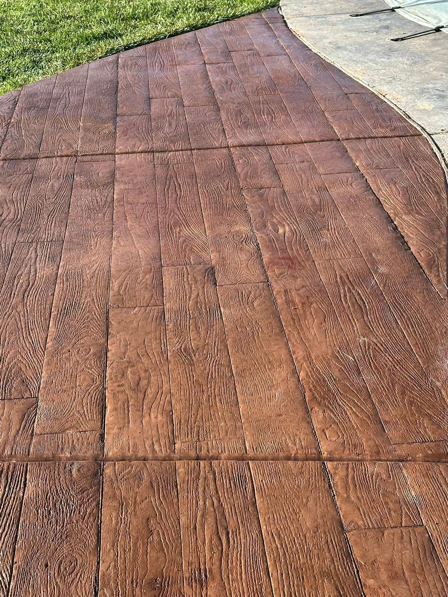 Stamped concrete walkway beside green grass and a light-colored pavement edge.