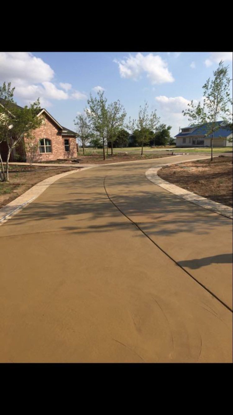 Curved paved road beside a brick house and trees under a partly cloudy sky
