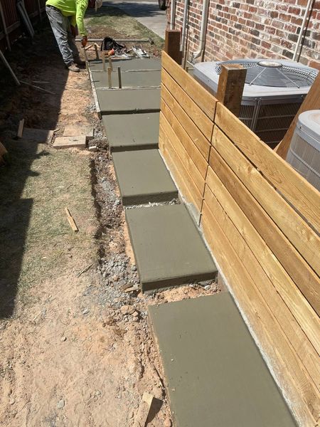 Fresh concrete steps along a narrow side yard beside a wooden fence and retaining wall.