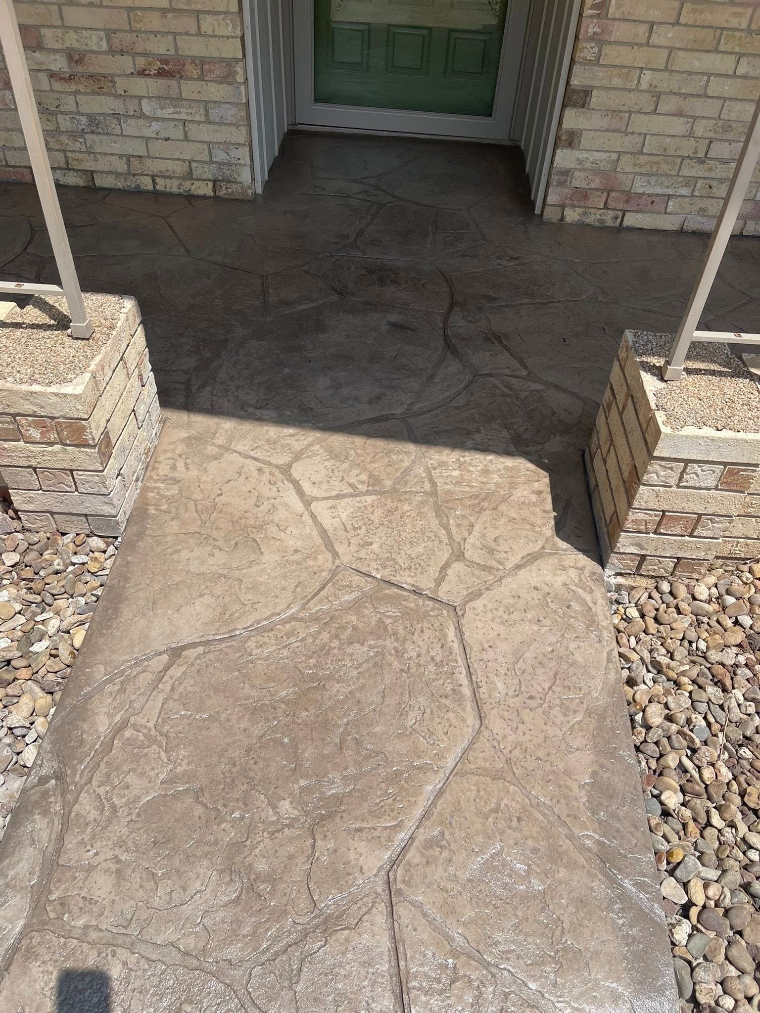 Cracked concrete walkway leading to a green front door between brick columns