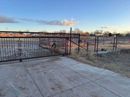 Snowy yard with a black metal gate and fence under a blue sky at sunset