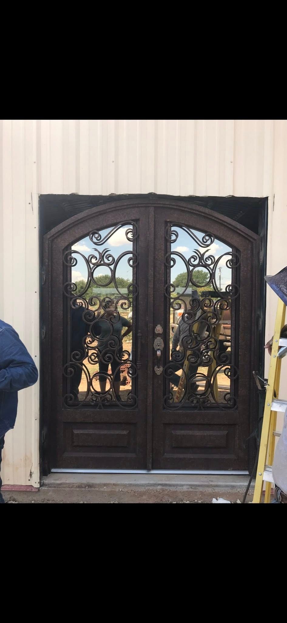 Dark wooden double doors with arched glass panels and reflections on a beige exterior wall.
