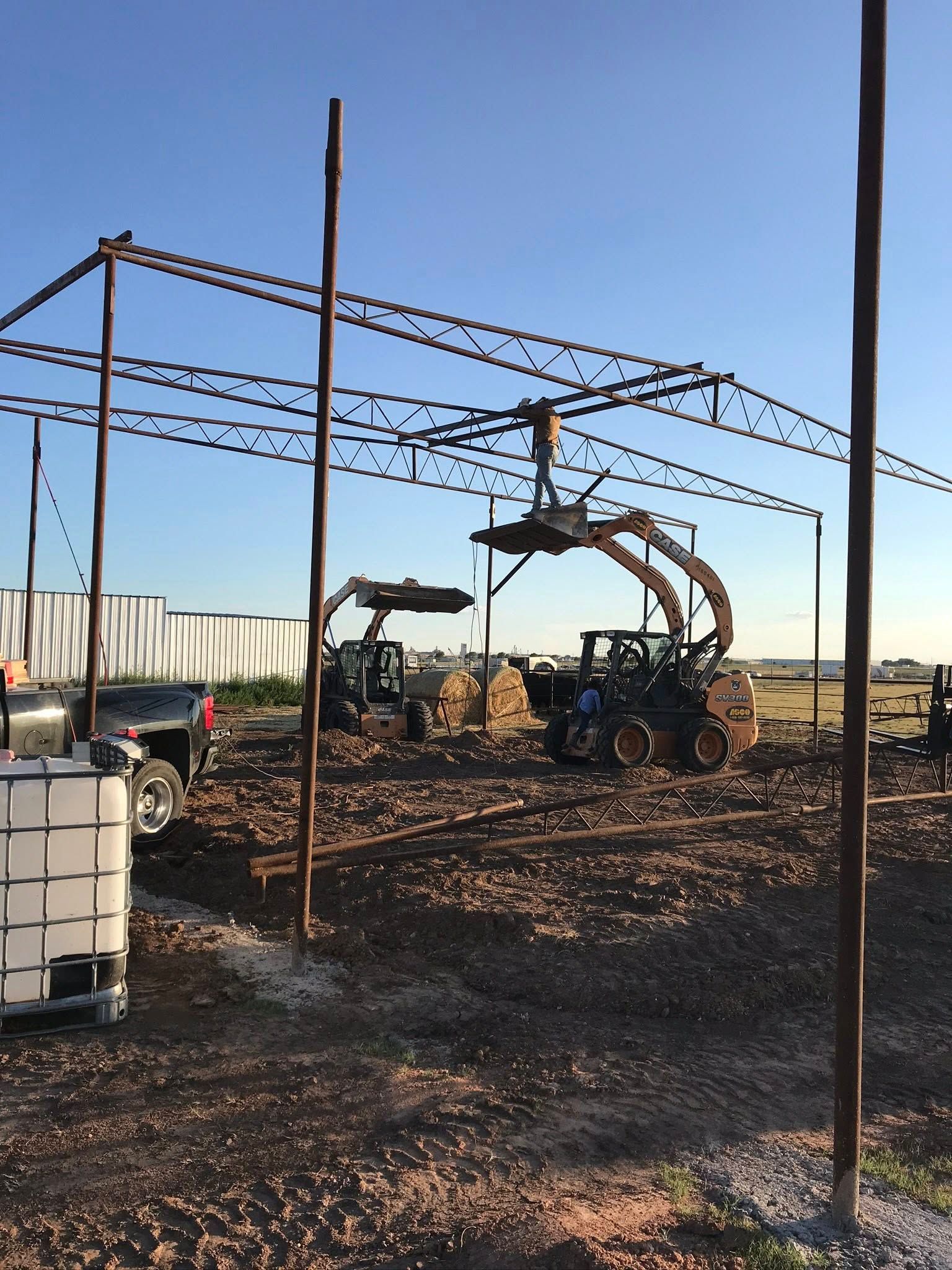 Farm equipment under a metal frame in a muddy field, with large tires and stacked materials nearby