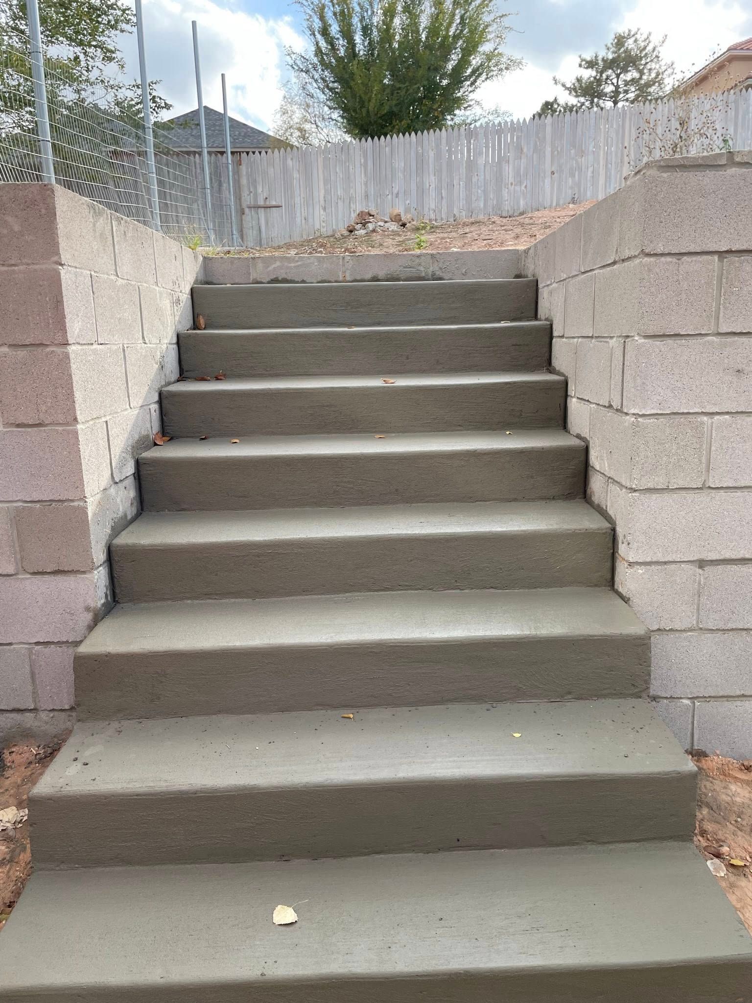 Concrete outdoor stairs between stone retaining walls leading up to a fenced yard