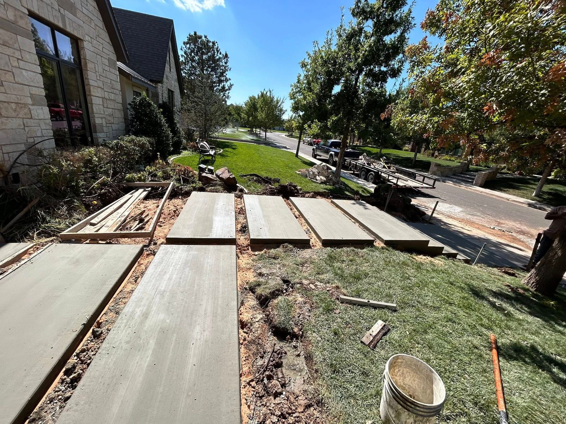 Pathway under construction beside a building, with concrete slabs laid over dirt and gravel, under a sunny sky