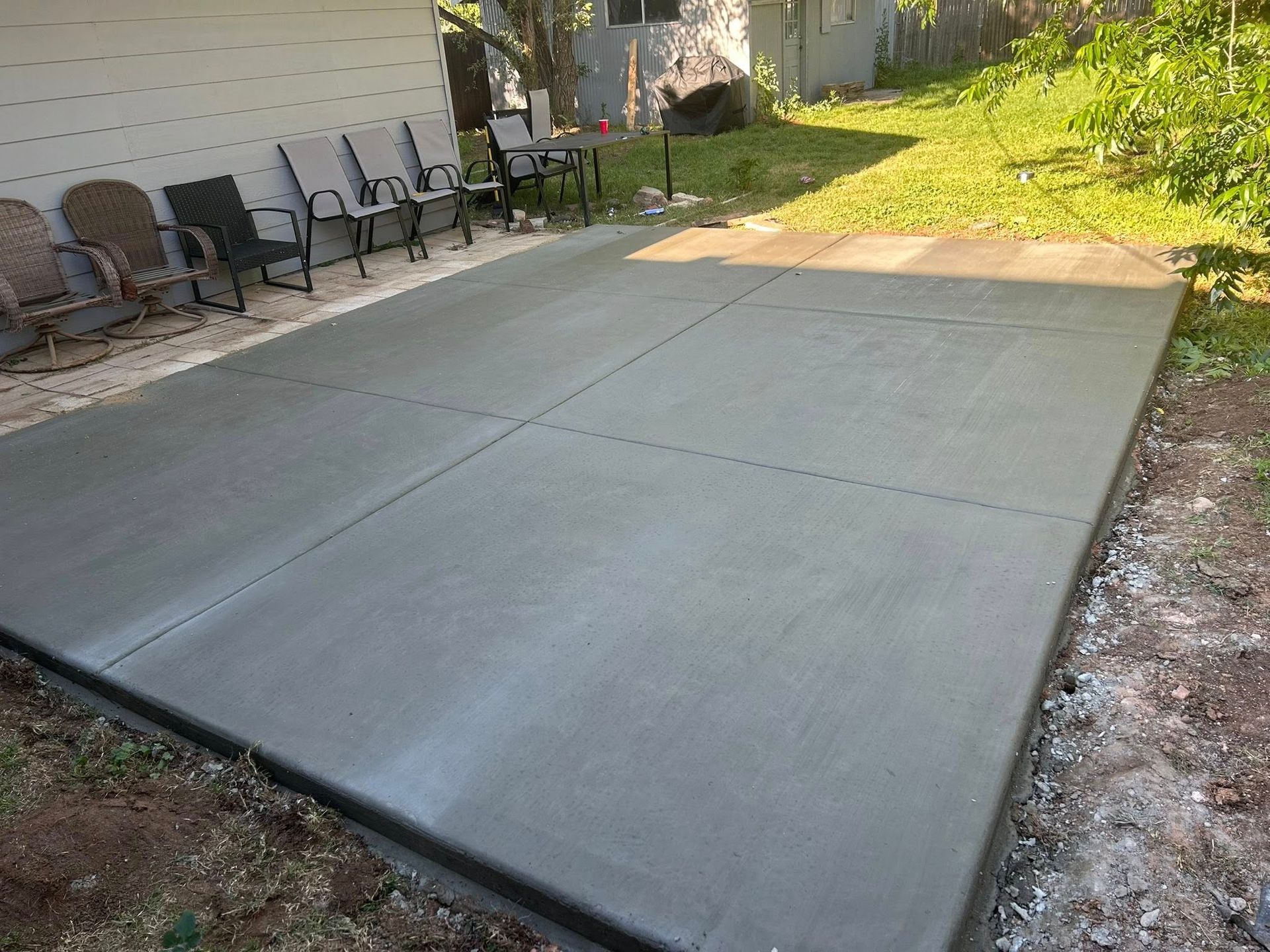 New concrete patio slab beside house, with outdoor chairs along the wall