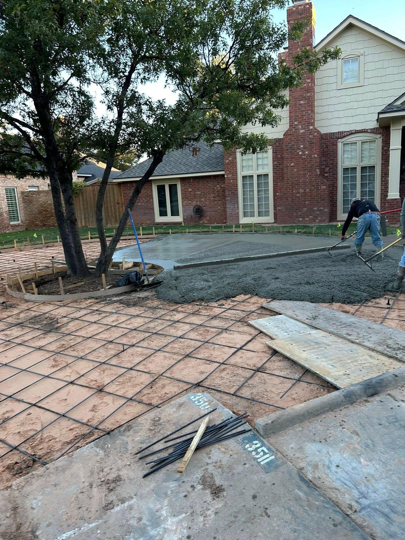 Residential driveway under construction with fresh gravel and pavers; worker shovels near a brick house.
