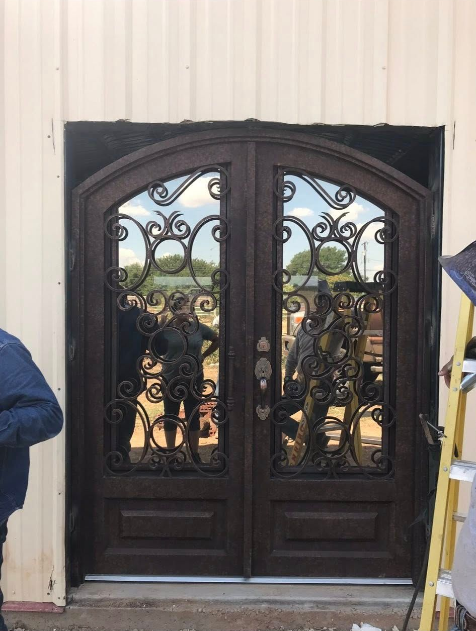 Ornate dark double front doors with decorative ironwork set in a light-colored building facade