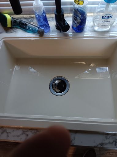 A kitchen sink with bottles of dish soap on the counter.