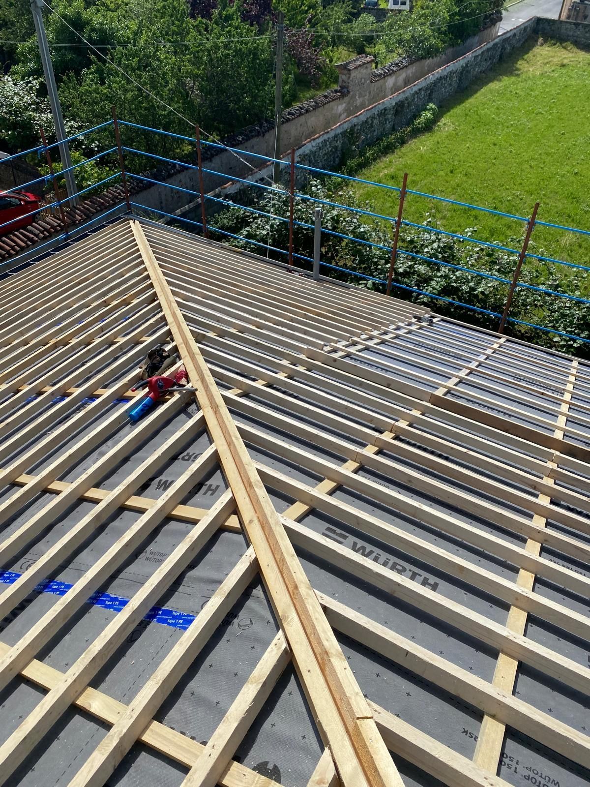 Vista di un tetto in costruzione con travi in legno, sottofondo nero e rete di sicurezza.