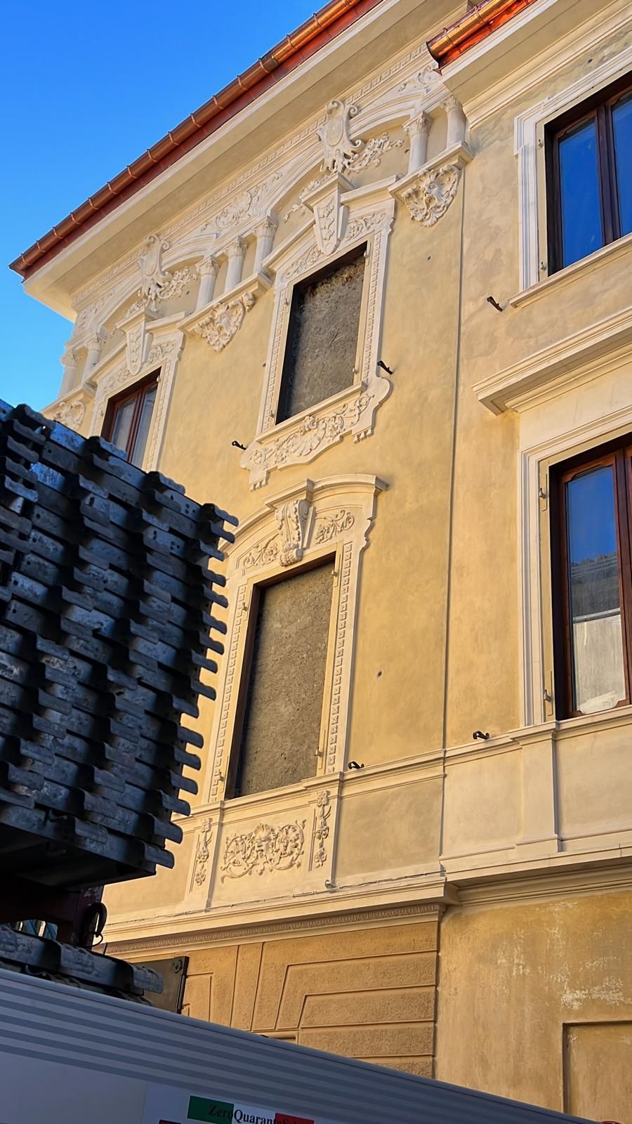 Edificio color crema decorato con rifiniture decorative, finestre con assi e materiali accatastati in primo piano.