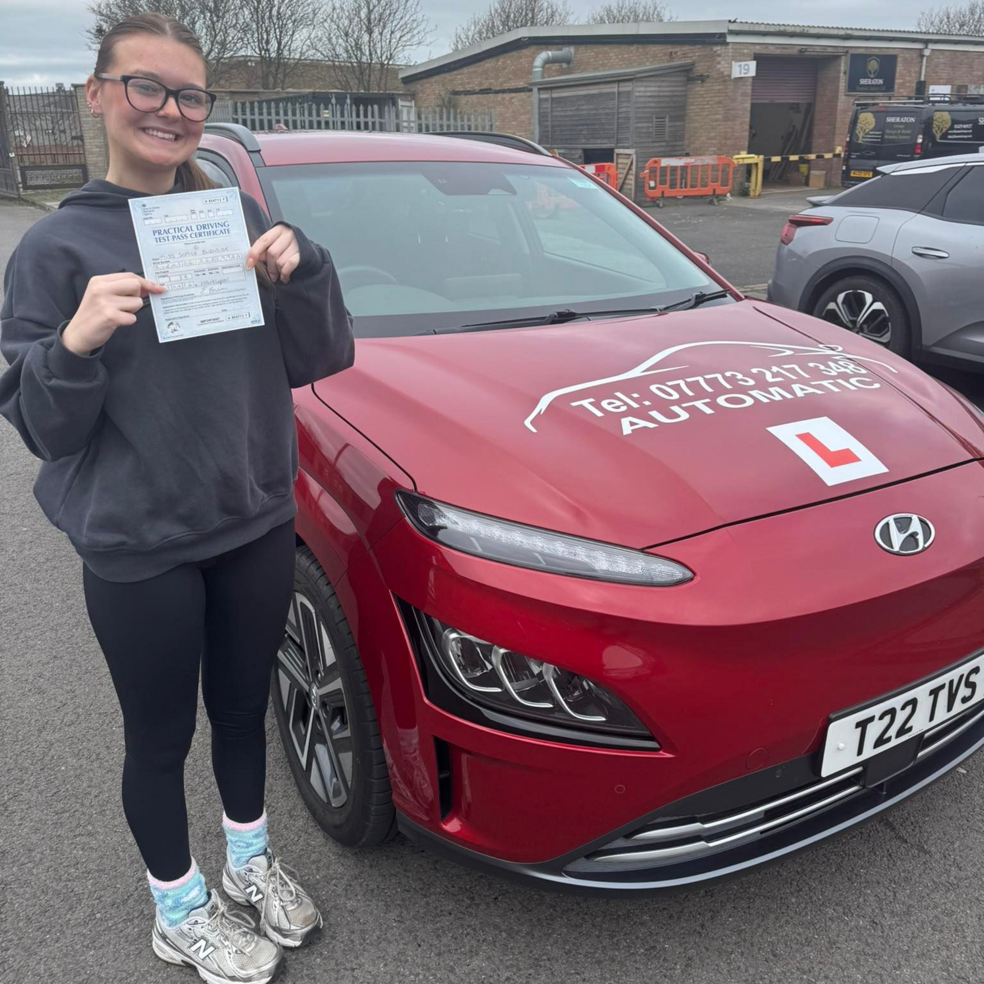 Person holding a paper beside a red driving school car in a parking lot
