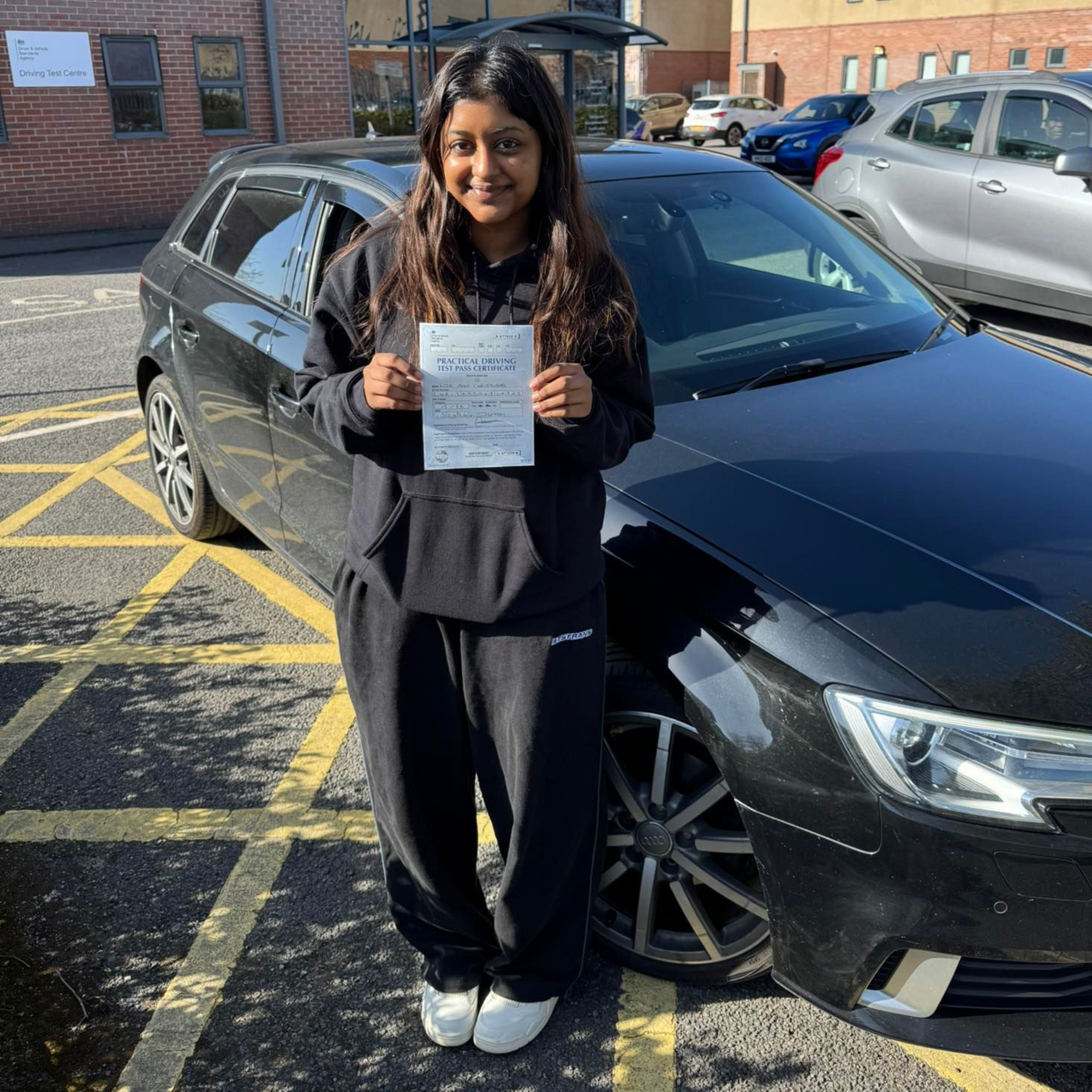 Person holding a paper in front of a black car in a parking lot.