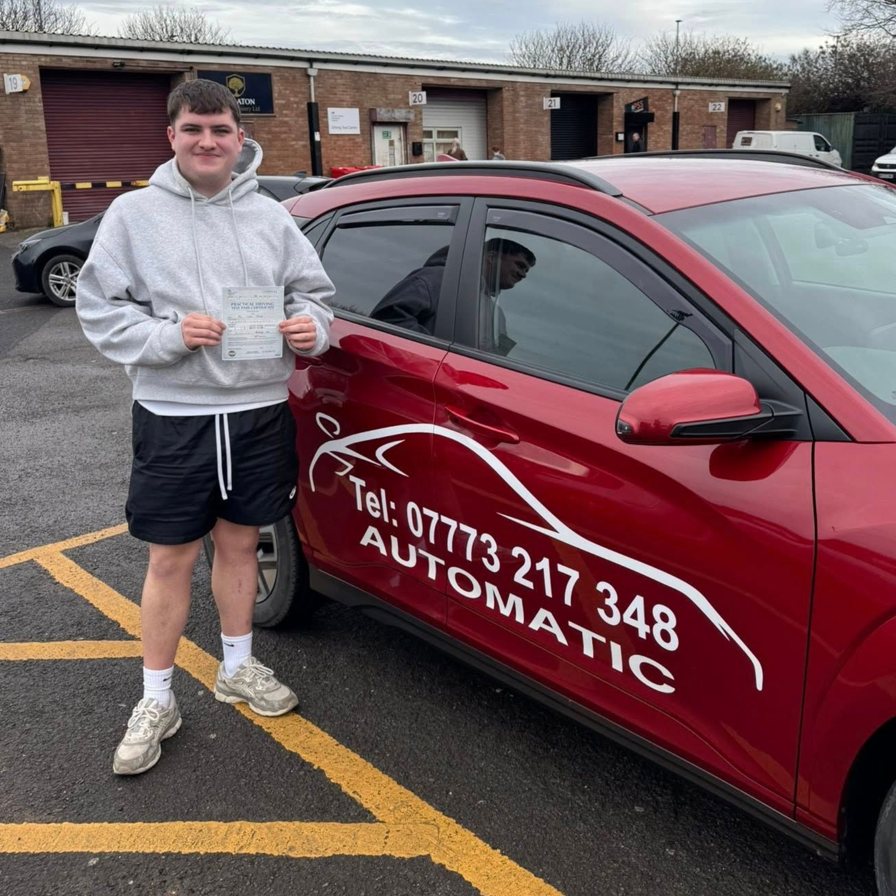 Person standing beside a red driving school car with “AUTOMATIC” and a phone number on the door.