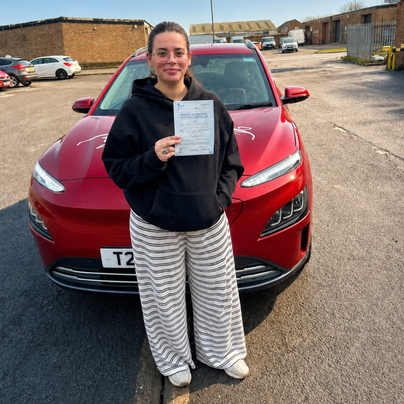 Person standing in front of a red SUV, holding up a document in a parking lot.