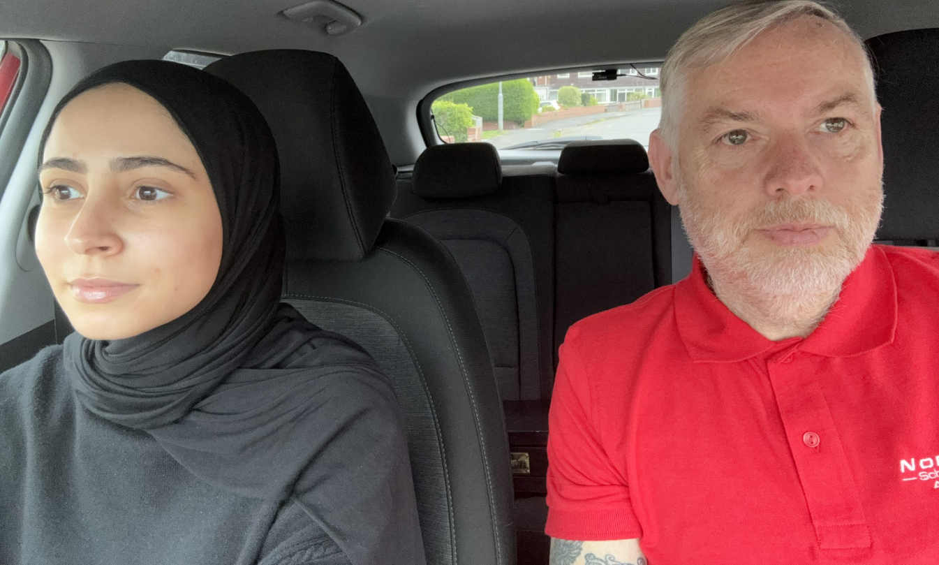Two people sitting in a car, one in a black headscarf and one in a red polo shirt.