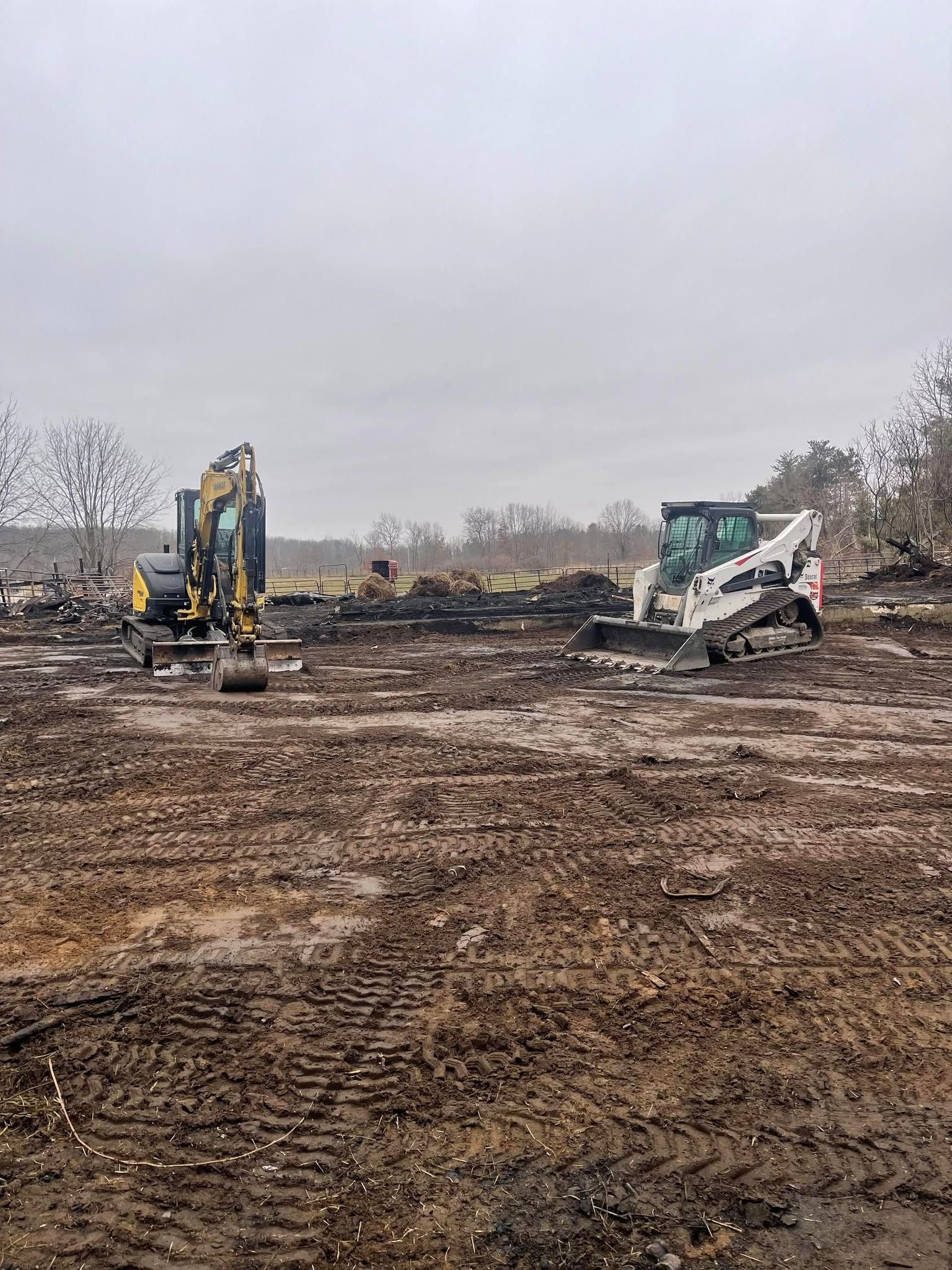 Construction site with two excavators on muddy ground under an overcast sky.