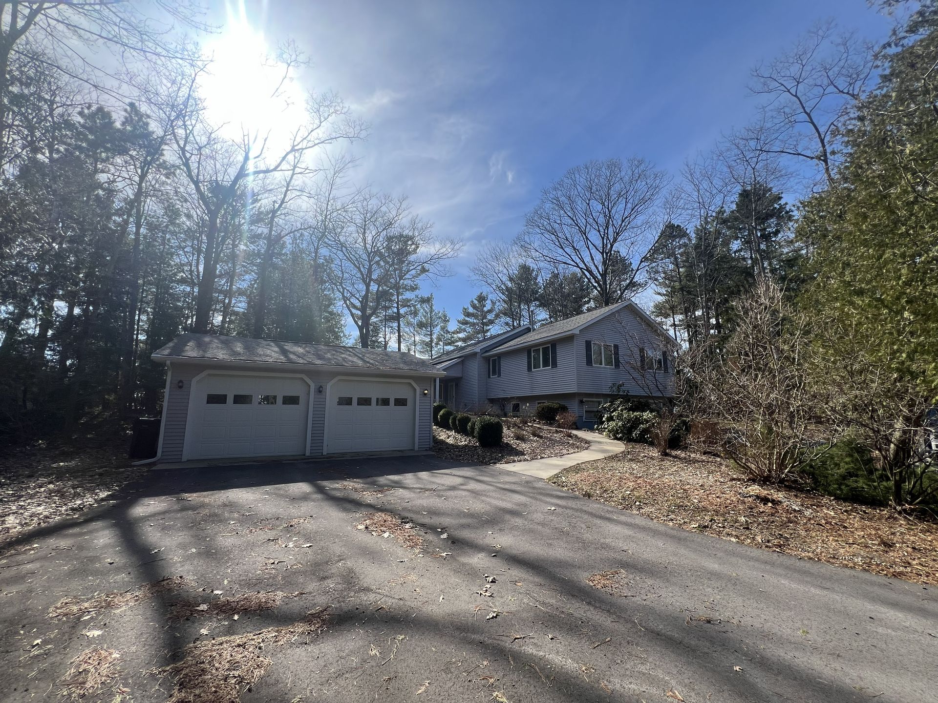 Driveway leading to a white two-car garage and house surrounded by trees on a sunny day