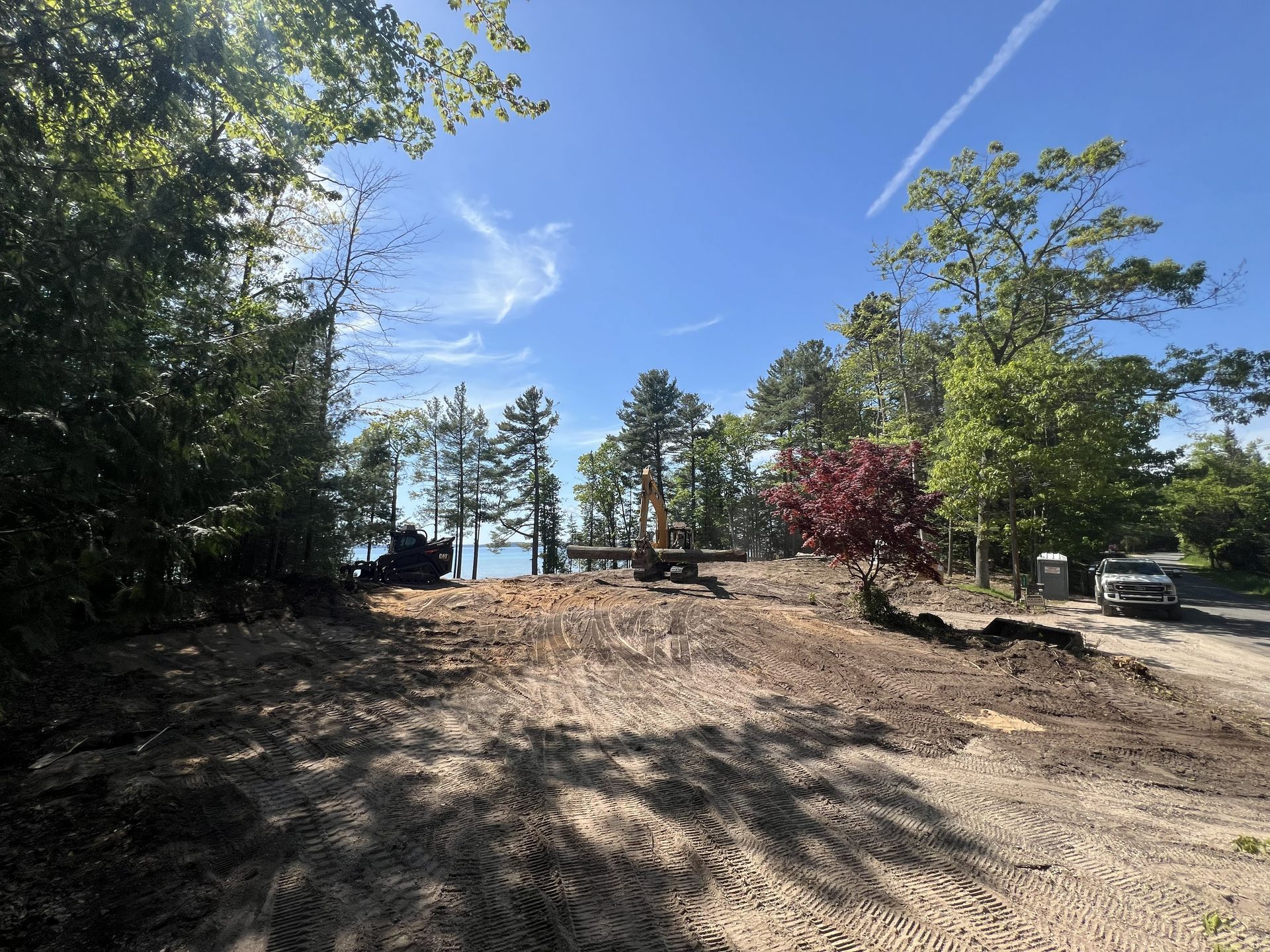 Dirt clearing with trees, blue sky, and a lake in the background