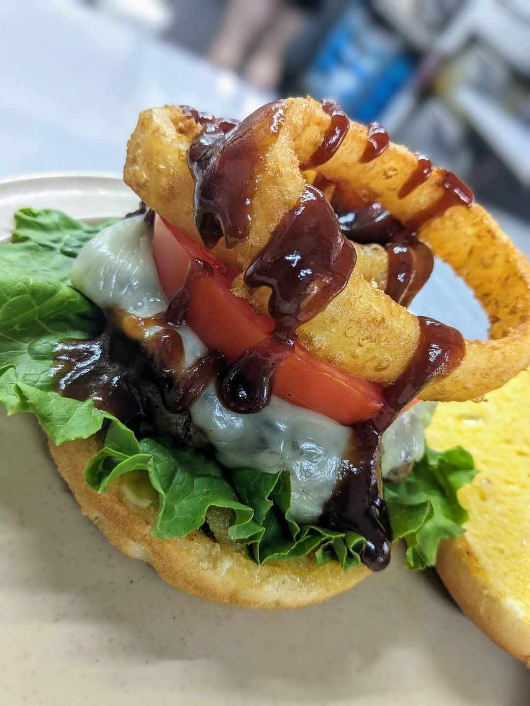A close up of a hamburger with onion rings on a plate.