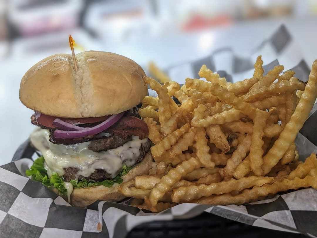 A hamburger and french fries on a checkered napkin on a table.