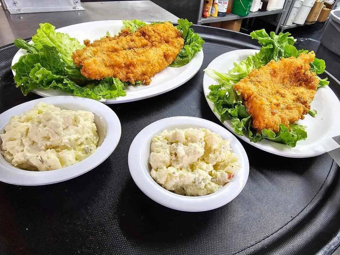 Three plates of food and two bowls of potato salad are on a tray.
