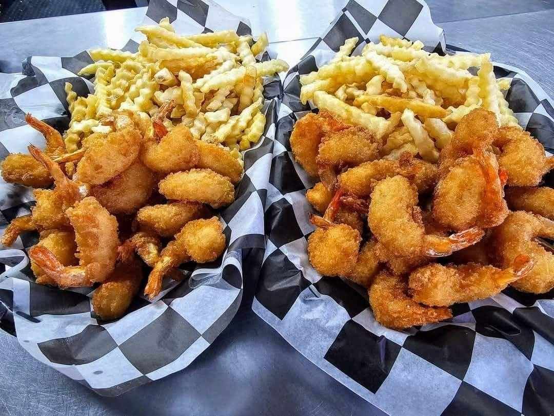 Two baskets of shrimp and french fries on checkered paper on a table.