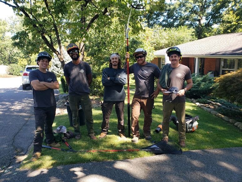Five people in black shirts pose with shovels on a suburban lawn in front of a house.
