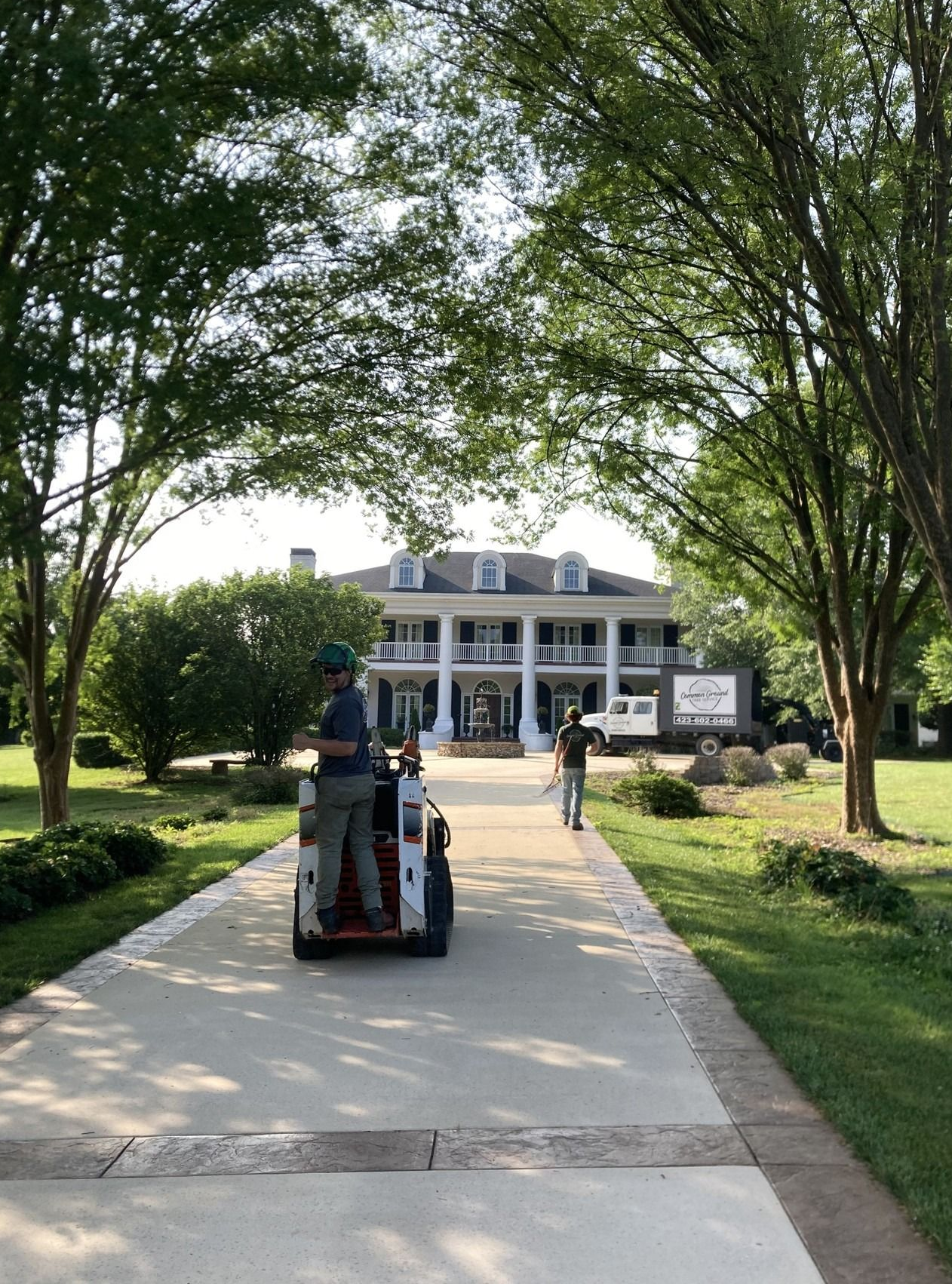 Tree-lined driveway leading to a white mansion, with a person riding a cart toward the entrance.