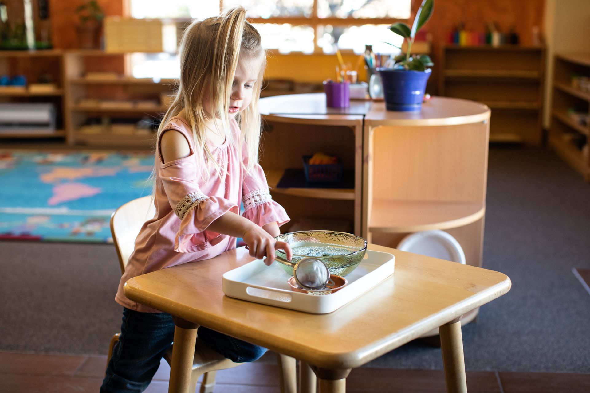 a little girl is sitting at a table playing with a tray .