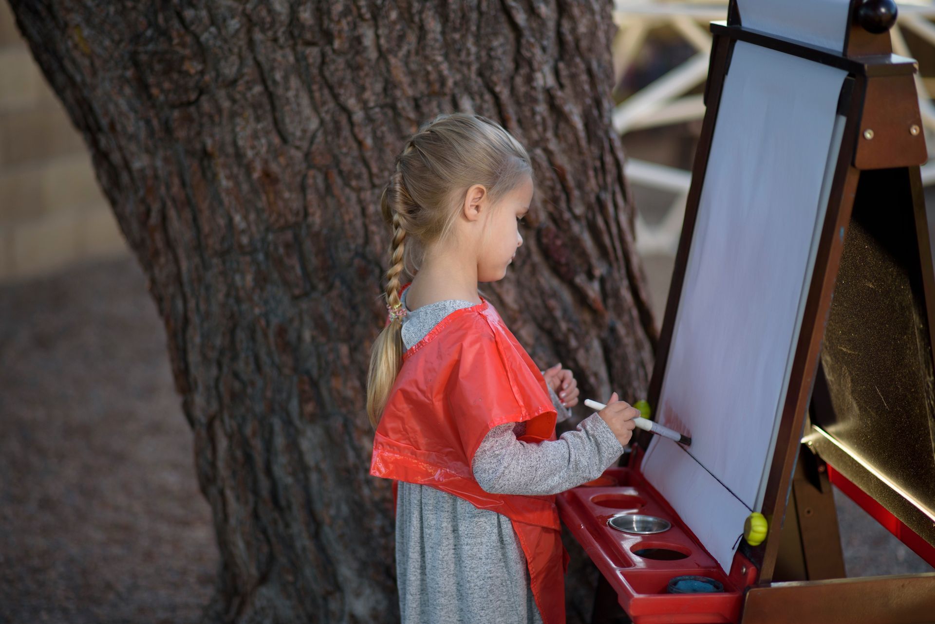a little girl is painting on an easel under a tree .
