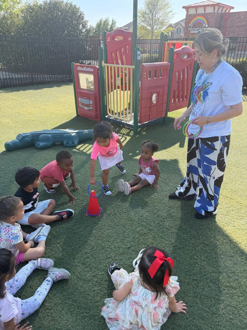 A Montessori teacher leads a group of toddlers in an outdoor ring toss game to develop coordination.