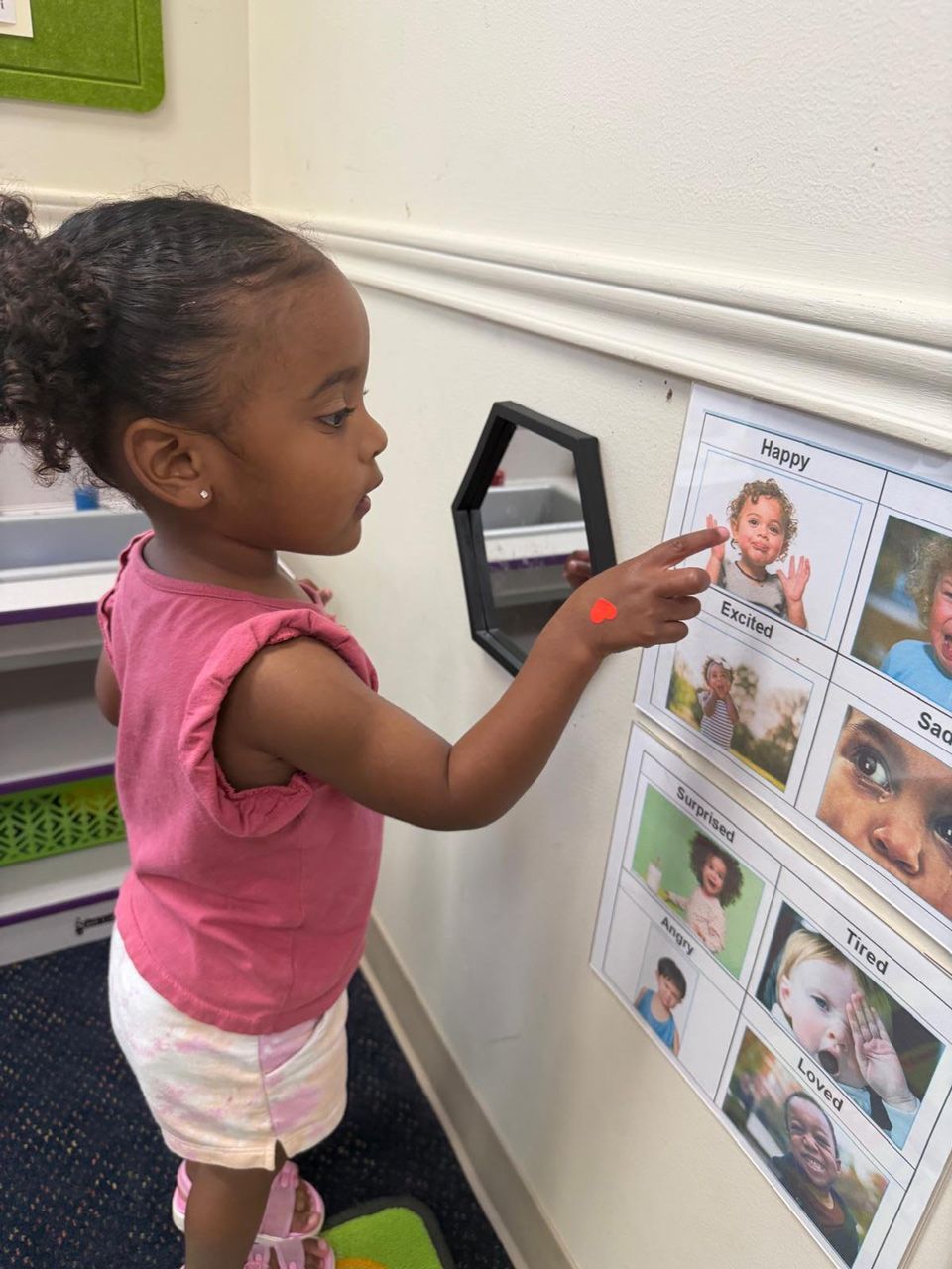 A toddler Montessori child points to an emotions chart on the wall to identify feelings as part of social-emotional development.